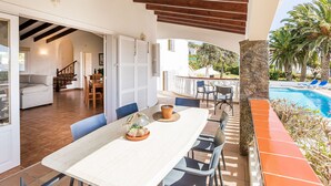 Un porche cubierto con mesa, sillas y vista a una piscina.