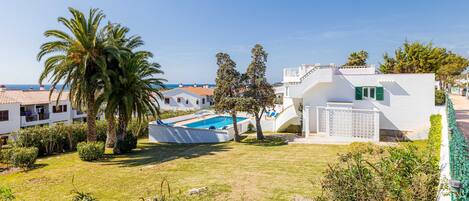 A white villa with a swimming pool, surrounded by greenery and a clear view of the sea.