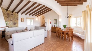 Un espacio habitable amplio con un sofá grande, una mesa de comedor y sillas, una pared de piedra y vigas de madera en el techo.