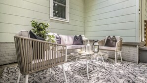 A cozy corner with a wicker chair, a cushioned bench, and a small round table with a bottle and glass.