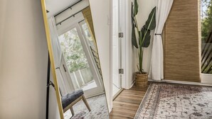 A modern interior with a bench, a large potted plant, a patterned rug, and a sliding door leading to a balcony.