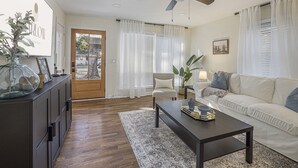 A living room with a dark wooden floor, a ceiling fan, a sofa, a coffee table, and a door leading outside.