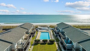 Une propriété située en bord de mer, dotée d’une piscine centrale, de plusieurs balcons et offrant une vue sur l’océan.