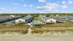 Un hôtel situé sur la côte, composé de plusieurs bâtiments à étages, doté d’une piscine centrale et offrant un accès à la plage.