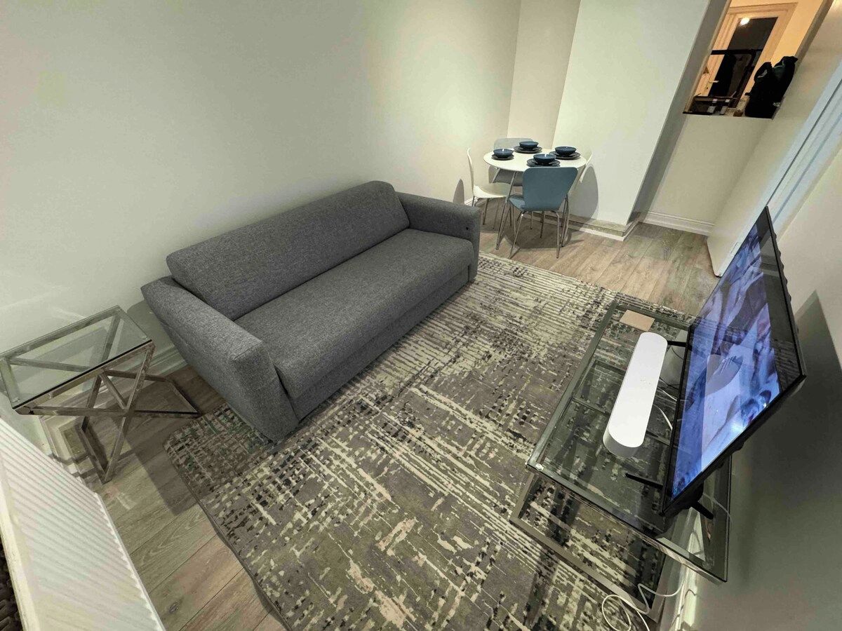 A living room with a gray sofa, a glass coffee table, and a flat-screen TV.