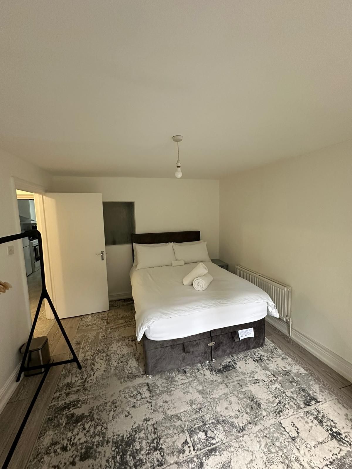 Une chambre à coucher comprenant un lit, un radiateur, un luminaire et une porte donnant sur une autre pièce.