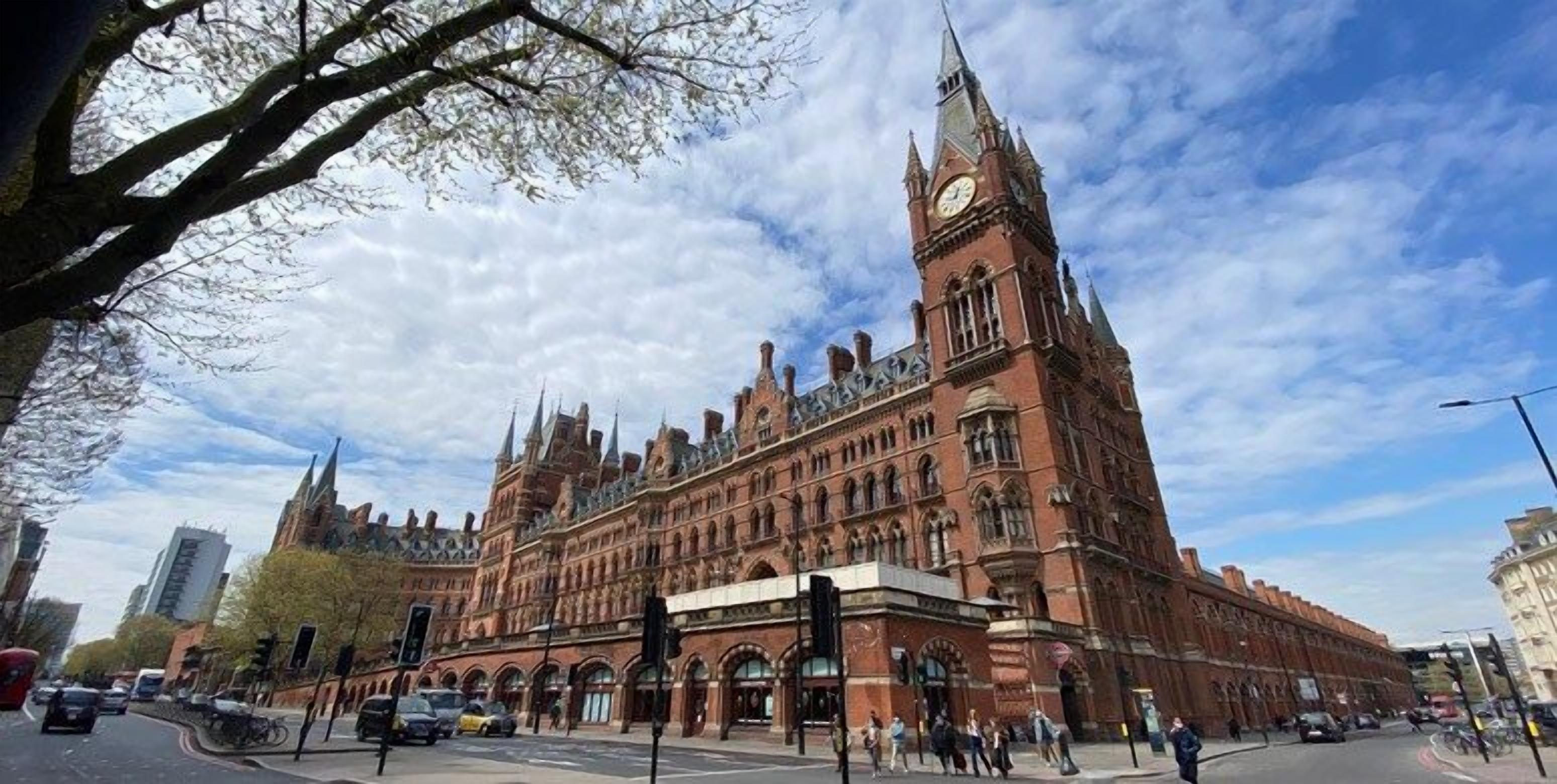 A large, historic building with a prominent clock tower, arched windows, and a central courtyard.