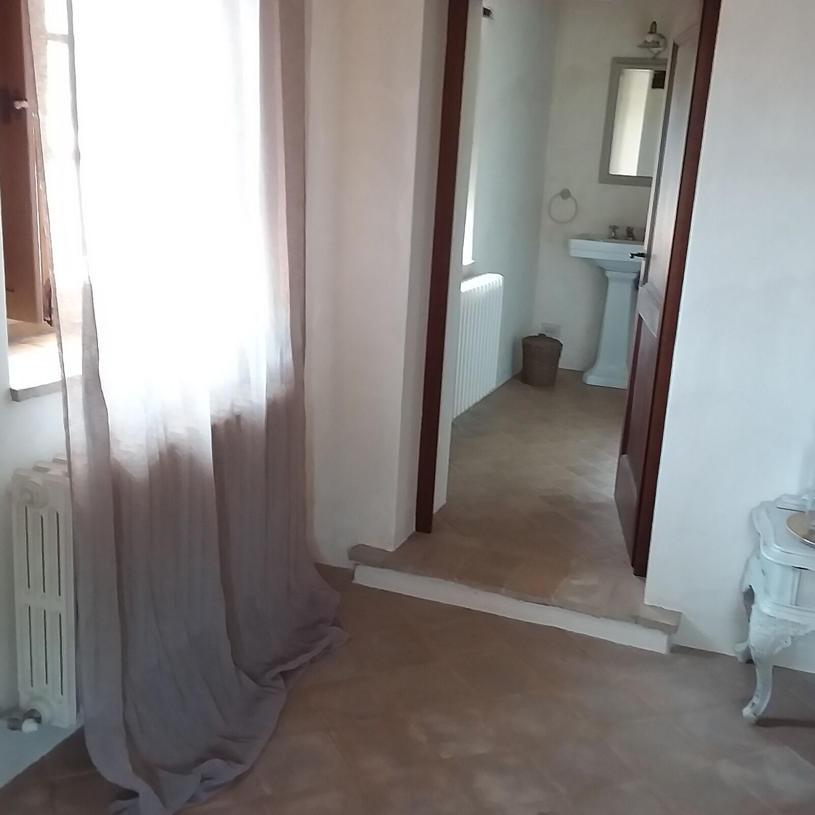A hallway with a radiator, a white sink, and a mirror on the wall.