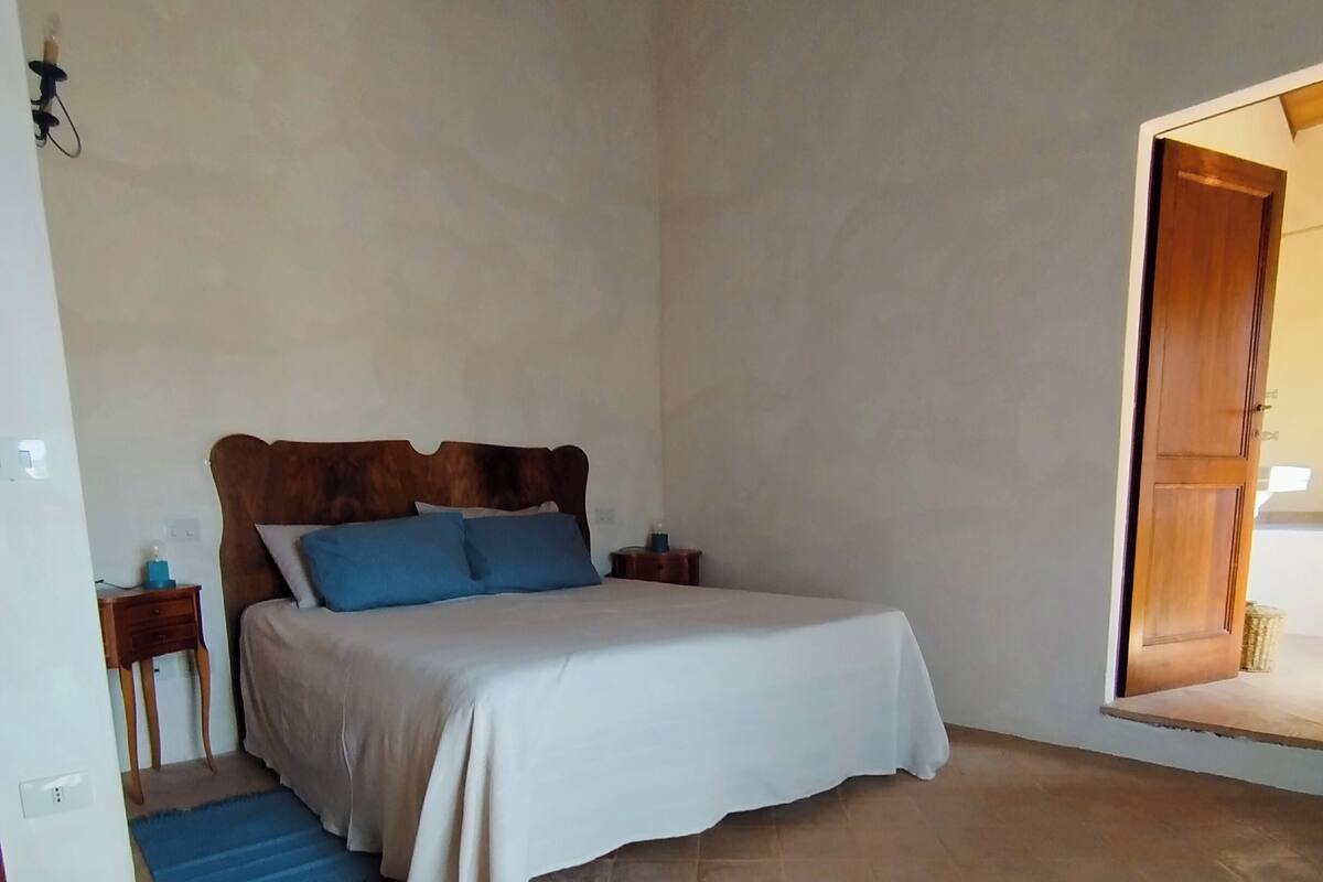 Een slaapkamer met een bed, een nachtkastje, een blauw tapijt en een houten deur.