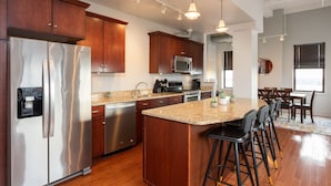 A modern kitchen with stainless steel appliances, wooden cabinets, and a central island with bar stools. - Skyline Square  (Niagara Falls)