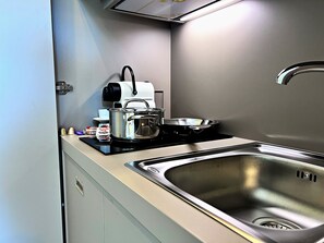 Una cocina compacta con un lavamanos de acero inoxidable, estufa y cafetera.