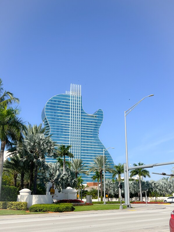 Un edificio moderno con diseño en forma de guitarra, rodeado de palmeras y un jardín bien cuidado.