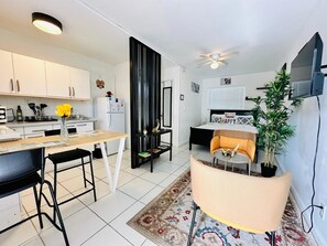 Una cocina moderna con armarios blancos, una mesa de comedor y una silla negra. Hay una planta pequeña en la mesa y un ventilador de techo.