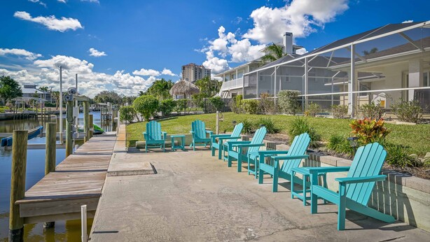 Une terrasse au bord de l’eau, agrémentée de chaises Adirondack turquoise, d’un quai et d’un bâtiment entièrement vitré.