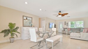 Un salon moderne avec une table à manger en verre, des canapés blancs, un ventilateur de plafond et une grande fenêtre.
