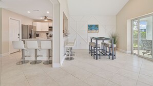 Une cuisine moderne avec des meubles blancs, un îlot central et un coin repas comprenant une table et des chaises.