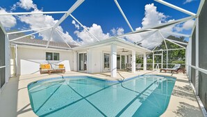 Une piscine dotée d’une enceinte en verre, entourée de mobilier d’extérieur et d’un patio couvert.