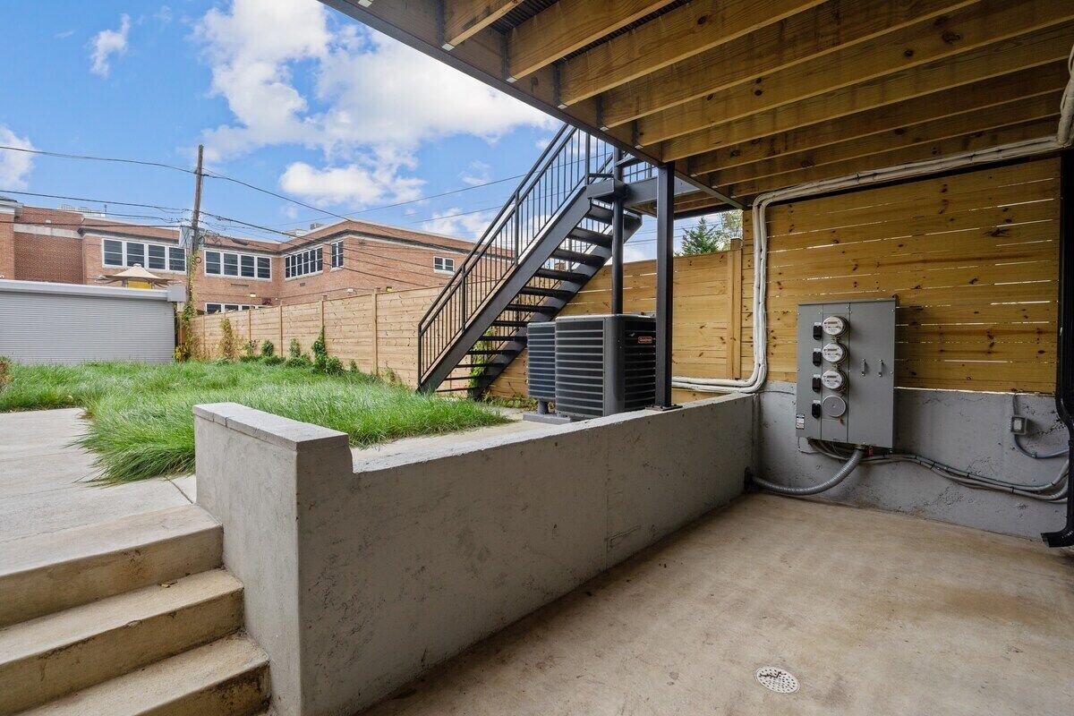 A concrete staircase leading to a wooden deck area with a metal railing, an air conditioning unit, and electrical panels.