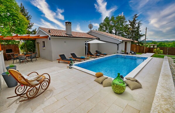Relax in a serene pool area surrounded by a patio with lounge chairs and a rocking chair.