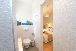 Cozy bedroom with a neatly made bed and a small plant, featuring a minimalist design.