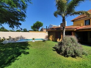 Ein Garten mit Swimmingpool, Rasen und einem Haus mit Ziegeldach.