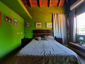 Ein Schlafzimmer mit Bett, grünen Wänden, Holzboden und einem Fenster mit Vorhängen.