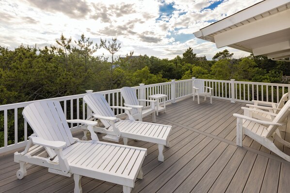 Una terraza de madera con sillas Adirondack blancas y barandilla blanca.