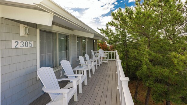 A wooden deck with white Adirondack chairs, a white railing, and a number sign '2305' on the building. - Brownley Beach Cottage- steps to the Beach, Elevator, Dog Friendly! (Virginia Beach)