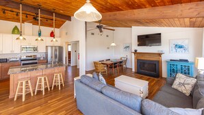 A spacious living area with a large gray sofa, wooden flooring, and a kitchen with modern appliances. - Brownley Beach Cottage- steps to the Beach, Elevator, Dog Friendly! (Virginia Beach)