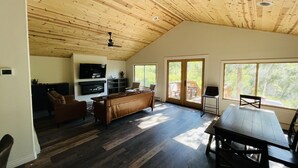 Amplia sala de estar con techo de madera, chimenea, televisor y mesa de comedor con sillas.