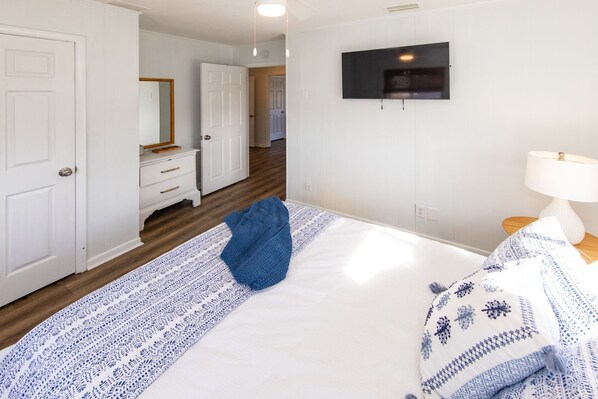 A hotel room with a bed, a TV mounted on the wall, a bedside table with a lamp, and a bathroom visible through an open door. - Easy Day- Pool, Hot Tub, Dog Friendly, Direct Beach Access! (Virginia Beach)