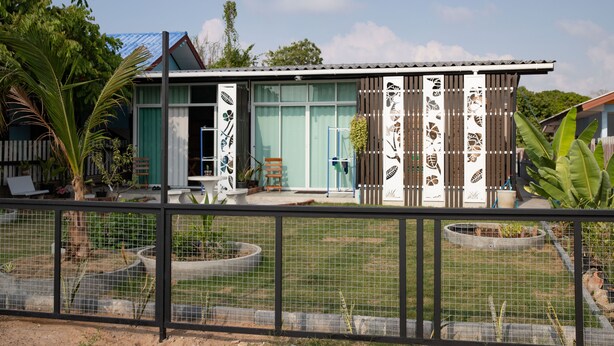 Una casa moderna con un amplio ventanal, un pequeño porche y un jardín vallado.