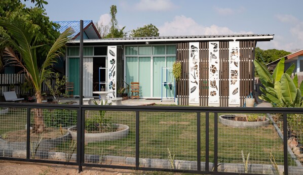 Una casa moderna con un amplio ventanal, un pequeño porche y un jardín vallado.