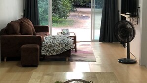 Una sala de estar con sofá, una mesa, un ventilador y una ventana con cortinas.