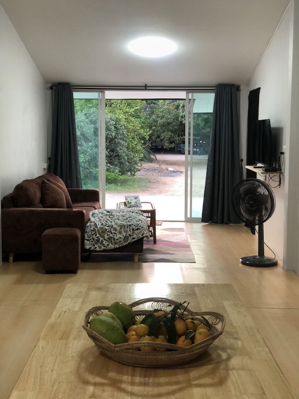Un soggiorno con divano, tavolo, ventilatore e finestra con tende.