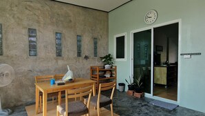 Una habitación con una mesa y sillas de madera, un reloj en la pared y un ventanal corredero que da a otra habitación.