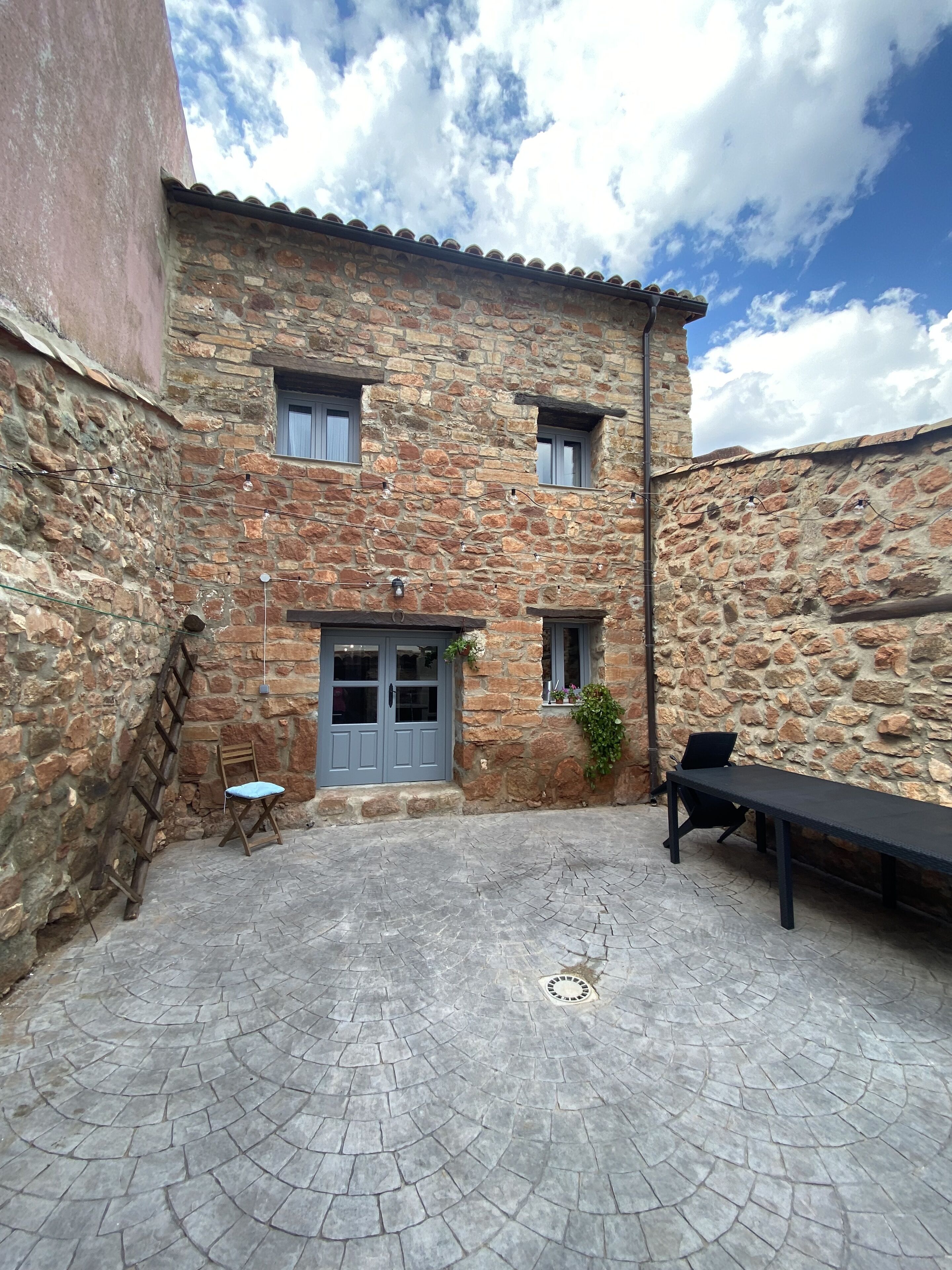 Un edificio in pietra con un cortile, una panchina, una sedia e una scala.