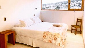 A bedroom with a bed, a wooden nightstand, a chair, and a window with a view of a snowy landscape. - Escalera al puerto Guest House  (Valparaiso)