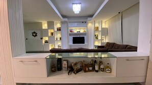 Een moderne woonkamer met een salontafel met glazen blad, een bruine bank en een aan de muur bevestigde televisie.