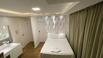 Ein Hotelzimmer mit einem großen Bett, einem Nachttisch, einem Spiegel und einem Vorhang.