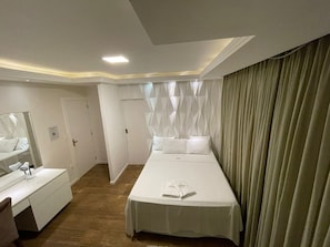A hotel room with a large bed, a bedside table, a mirror, and a curtain. - Pousada Mineira SJB (Sao Joao Da Barra)