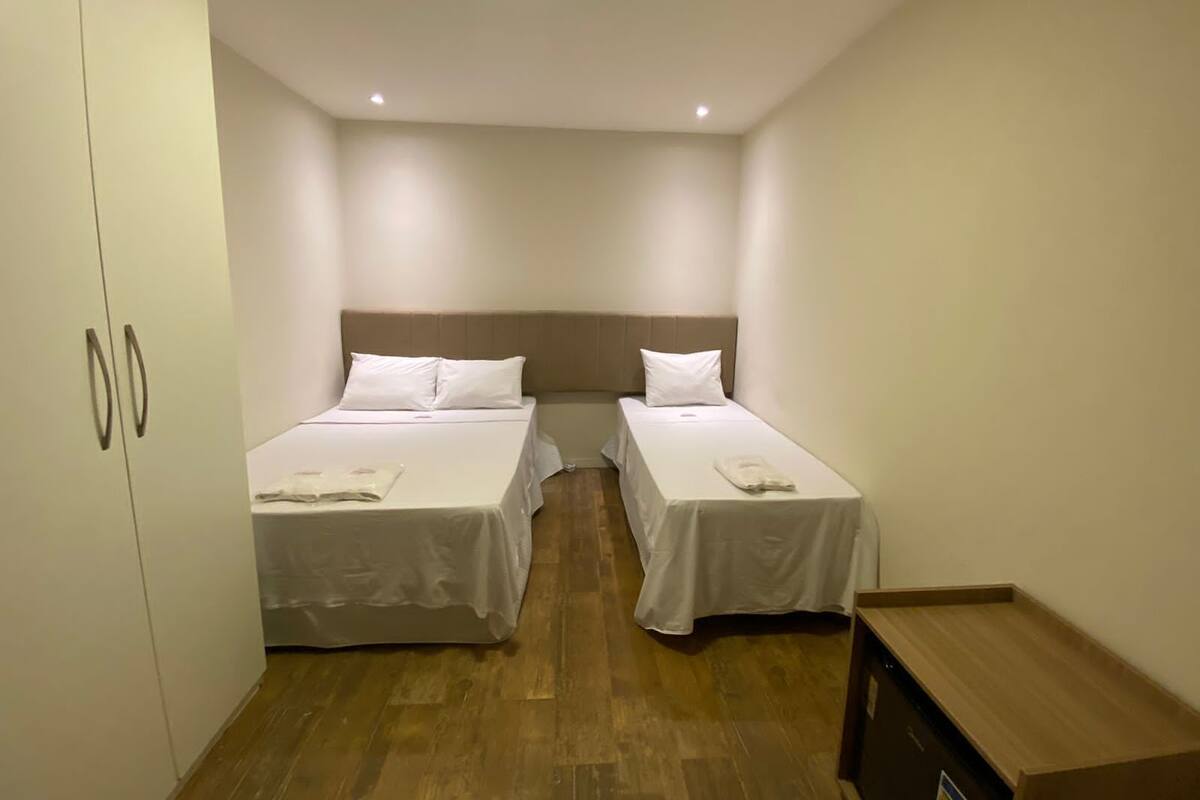 Quarto de hotel com duas camas, piso de madeira e um guarda-roupa.