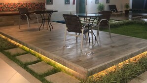 Een terras buiten met een eettafel en stoelen, een overdekte zithoek, en een bordje met de tekst 'Mineira'.