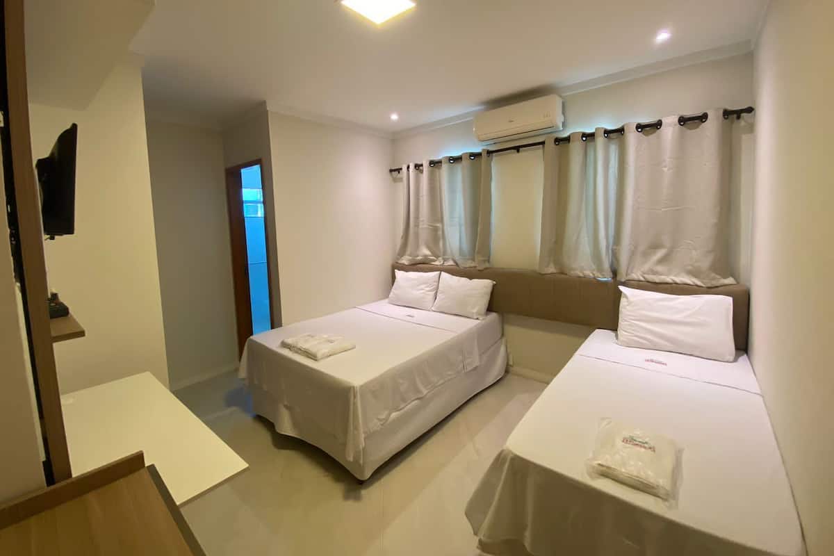 Quarto de hotel com duas camas de solteiro, uma mesa pequena, televisão e ar condicionado.