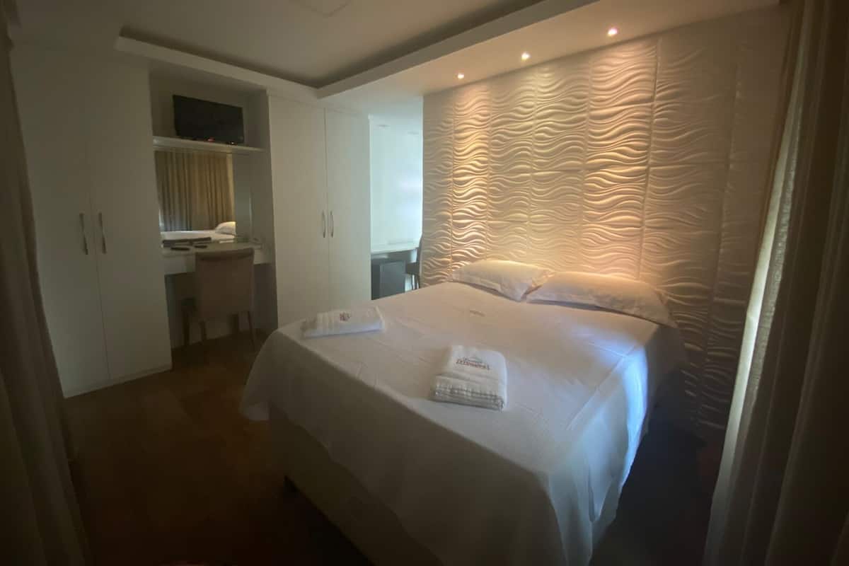 Quarto de hotel com cama, escrivaninha e guarda-roupa.