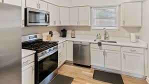 A modern kitchen with white cabinets, stainless steel appliances, and a window with blinds. - Modern Home near DT Libertyville and Naval Base (Libertyville)