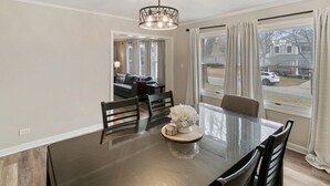 A dining area with a dark wooden table, chairs, a chandelier, and a view of the outside through large windows. - Modern Home near DT Libertyville and Naval Base (Libertyville)
