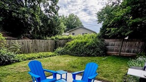 A patio with blue Adirondack chairs and a table, surrounded by a wooden fence and greenery. - Modern Home near DT Libertyville and Naval Base (Libertyville)
