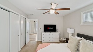 A hotel room with a bed, a TV, a ceiling fan, a dresser, and a window with blinds. - Modern Home near DT Libertyville and Naval Base (Libertyville)