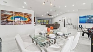 Un espace repas moderne avec une table en verre, des chaises blanches et un grand tableau abstrait accroché au mur.